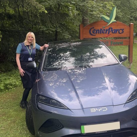 Laura Dunsmoir, driver from Center Parcs, stood next to her grey BYD Seal in front of her Center Parcs workplace sign