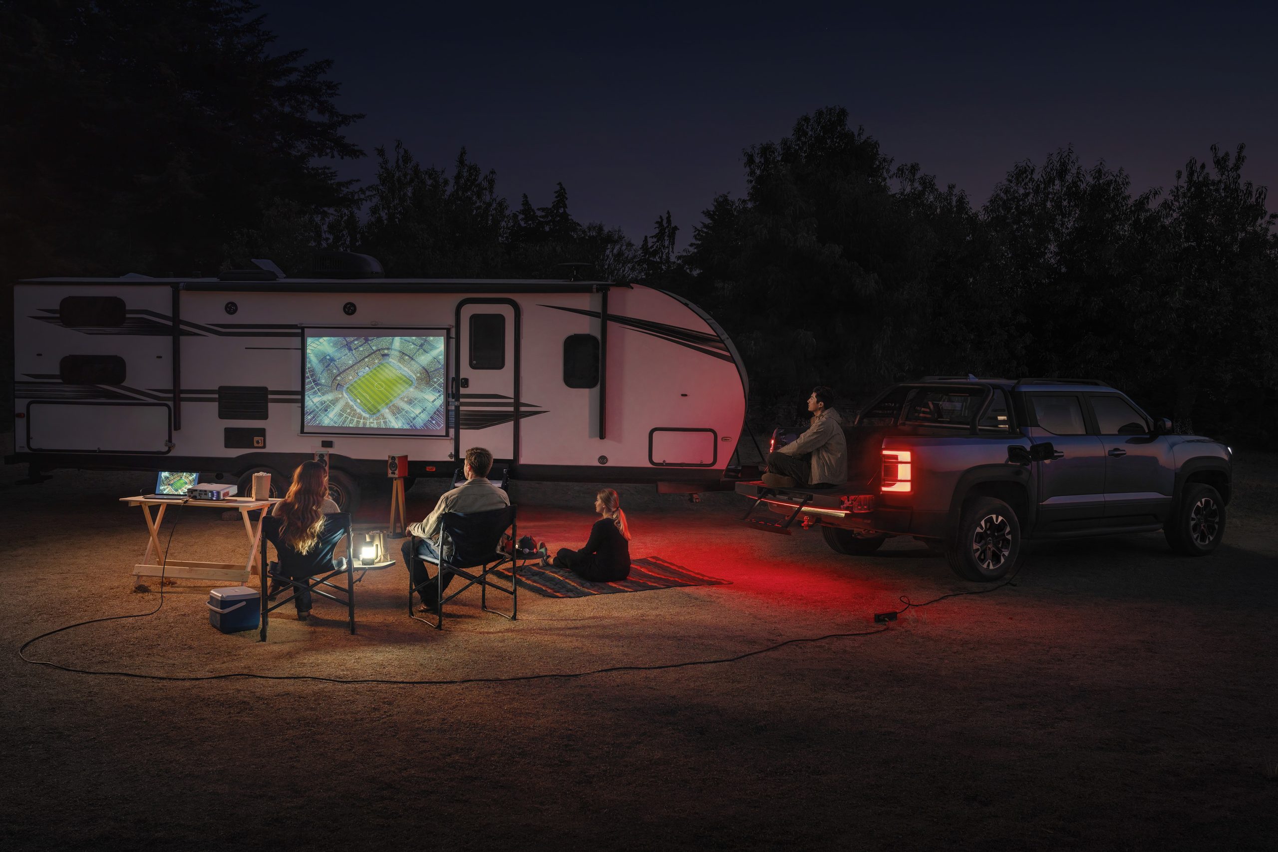 Family sat watching football on a projector screen outside whilst using bidirectional, V2L charging to power external products.