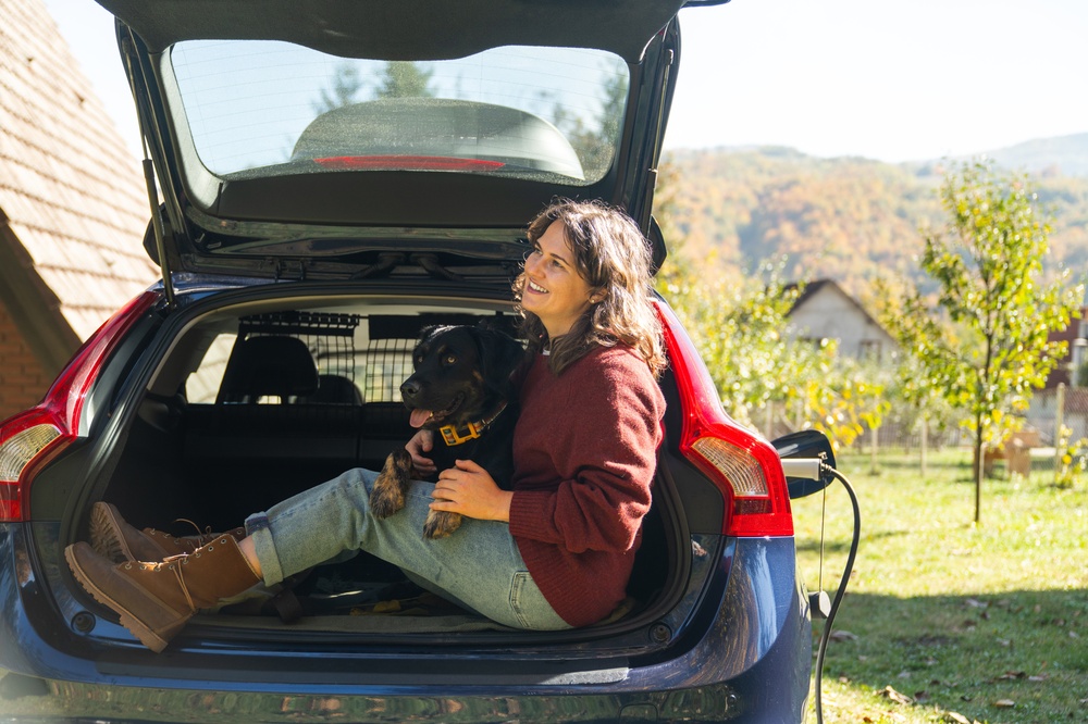 women sitting in boot with her dog showing the dog guard attached to the boot for dog safety in the car